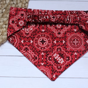 May include: Red bandana with a black and white paisley pattern. The bandana has a gathered elastic band at the top.