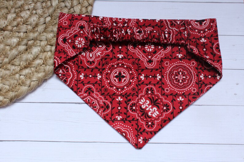 May include: Red bandana with a black and white paisley pattern. The bandana has a gathered elastic band at the top.