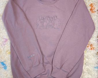 May include: A mauve sweatshirt with a line drawing of a group of people on the front. The sweatshirt has the word "Liam" embroidered on the left sleeve.
