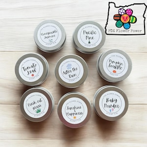 May include: Ten round metal tins with colorful labels and illustrations. The labels include the text "PDX Flower Power" and the names of different scents, such as "Honeysuckle Jasmine", "Pacific Pine", "Tomato Leaf", "After the Rain", "Fresh Cut Grass", "Sunshine & Happiness", "Pumpkin Souffle", and "Baby Powder".