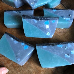 May include: Six bars of handmade soap with a blue and gray marbled design. The soap is cut into rectangular shapes and has a black stripe across the top.