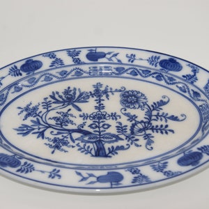 May include: A white oval serving platter with a blue floral design. The design features a central tree with branches and leaves, surrounded by smaller floral motifs. The platter has a blue border with a repeating pattern of stylised flowers and leaves.