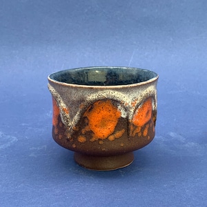 Könnte beinhalten: Eine Keramikschale mit dunkelbraunem Boden und ausgestelltem Rand. Die Schale hat ein strukturiertes Design mit orangefarbenen und weißen Akzenten. Der Innenraum ist dunkelblau. Die Schale ist etwa 10 cm hoch.