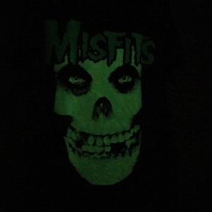 May include: Green glow-in-the-dark Misfits skull graphic on a black background.