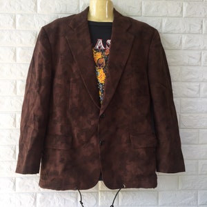 Puede incluir: Una chaqueta marrón con estampado de camuflaje. La chaqueta tiene cierre de dos botones y un cordón en la parte inferior.