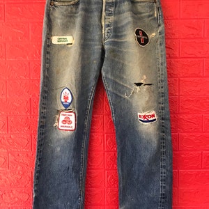May include: Blue denim jeans with multiple patches, including "Central Services", "Camaro", "State Farm Insurance", "Exxon", and a Maserati logo.
