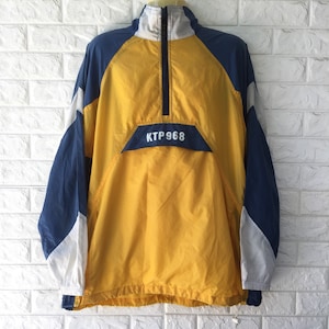 May include: A yellow, navy blue, and white anorak jacket with a half-zip closure. The jacket features the text "KTP 968" on the front and a drawstring at the hem. The sleeves are navy blue and white, and the body is yellow.
