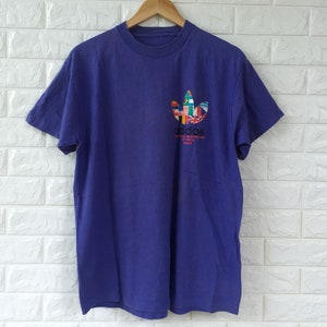 May include: A purple short-sleeved t-shirt with a white Adidas logo made up of flags from around the world. The text "adidas World Cup 1994" is printed below the logo.