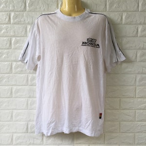 May include: White t-shirt with black and white stripes on the sleeves. The shirt has a black Honda logo with the text "Grand Prix Racing Team" underneath.
