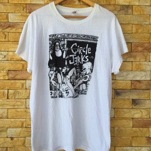 May include: White t-shirt featuring a black and white graphic print of a band called "Circle Jerks".