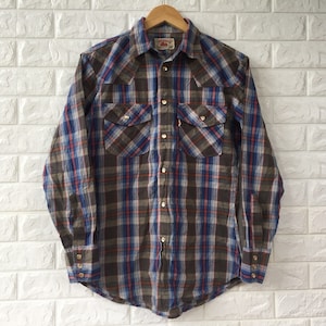 May include: A long-sleeved plaid shirt with a brown, blue, and red plaid pattern. The shirt has a button-down collar, two chest pockets, and a single button cuff.