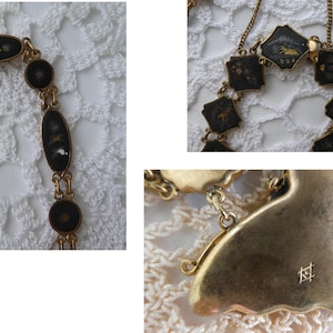 Op de afbeelding: Een gouden ketting met zwarte emaille hangers met ingewikkelde ontwerpen. De ketting heeft een sluiting met de inscriptie "K24".