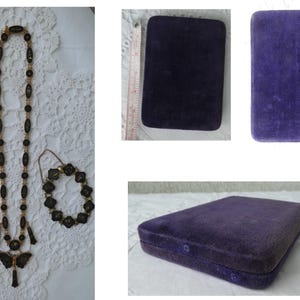 Op de afbeelding: Een zwarte en gouden ketting- en armbandset met een vlinderhanger. De set wordt getoond op een witte kant achtergrond en wordt geleverd in een paarse fluwelen doos.