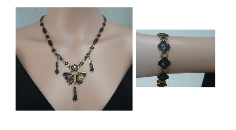 Op de afbeelding: Een gouden ketting met een zwarte vlinder hanger en zwarte en gouden accenten. De ketting is om de nek van een model. Een bijpassende armband met zwarte en gouden accenten is om de pols van een model.