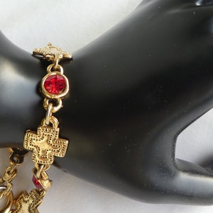 May include: Gold bracelet with red crystal accents and cross charms.