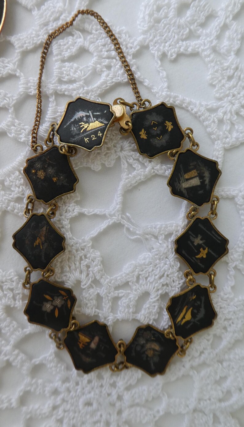 Op de afbeelding: Een gouden kettingarmband met zwarte emaille bedels met Japanse sc&egrave;nes in goud. De bedels zijn verbonden door gouden schakels. De armband heeft een sluiting met de markering "K 24".