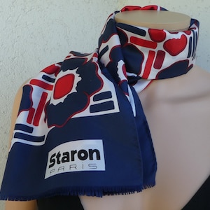 Puede incluir: Un pañuelo azul marino, rojo y blanco con un estampado floral geométrico. El pañuelo tiene un borde con flecos y el texto "Staron PARIS" en un rectángulo blanco. El pañuelo está drapeado alrededor del cuello de un maniquí.