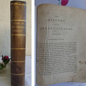 Könnte beinhalten: Ein antikes Buch mit dem Titel "History of the Orkney Islands". Es hat einen braunen Ledereinband mit goldener Schrift und goldenen Bändern. Die offenen Seiten zeigen Text aus der Einleitung. Ein historisches Objekt.