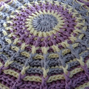 Peut inclure: Gros plan d'une dentelle ronde au crochet avec un centre violet clair et un motif de fils alternés violet clair et crème.