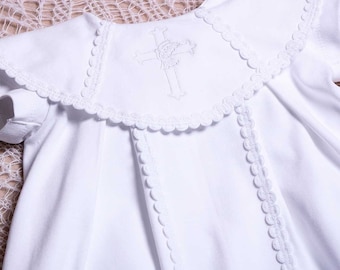 May include: White baby gown with a scalloped collar and embroidered cross on the front.