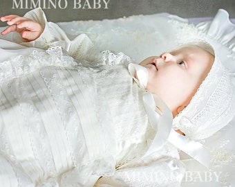 May include: A white baby christening gown with lace detailing and a matching bonnet. The gown has a ruffled neckline and a long, flowing skirt. The bonnet is trimmed with lace and has a bow on top.