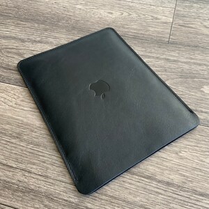 May include: Black leather sleeve with a stitched edge and an Apple logo in the center.