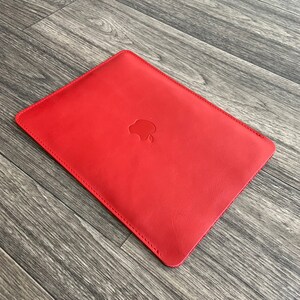 May include: Red leather laptop sleeve with an Apple logo embossed on the front.