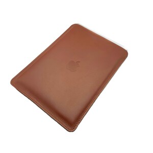 May include: A brown leather sleeve with a stitched edge and an embossed Apple logo.
