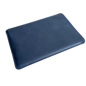 May include: A navy blue leather laptop sleeve. The rectangular case has rounded corners and is stitched with white thread around the edges. The sleeve is designed to protect a laptop.