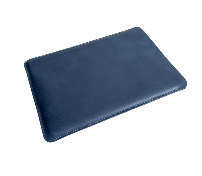 K&ouml;nnte beinhalten: Eine marineblaue Laptop-H&uuml;lle aus Leder. Die rechteckige H&uuml;lle hat abgerundete Ecken und ist mit wei&szlig;em Faden an den R&auml;ndern gen&auml;ht. Die H&uuml;lle dient zum Schutz eines Laptops.