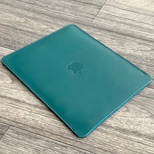 May include: A teal leather laptop sleeve with a stitched edge and an Apple logo embossed on the front.