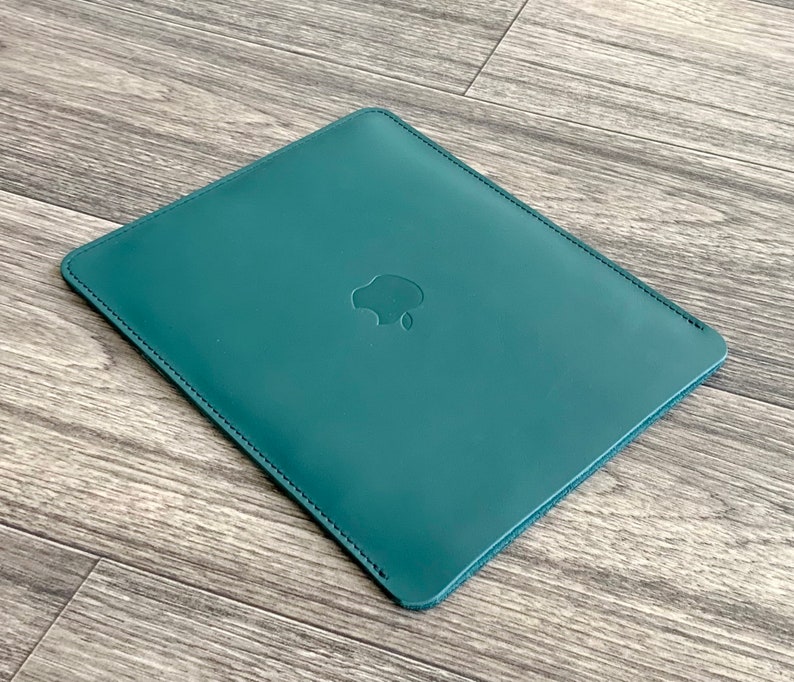 May include: A teal leather laptop sleeve with a stitched edge and an Apple logo embossed on the front.