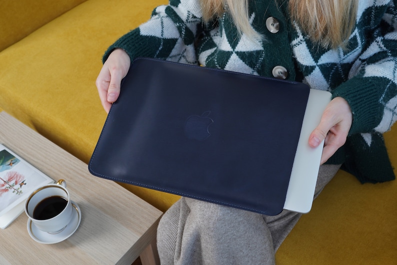 K&ouml;nnte beinhalten: Eine dunkelblaue Laptoptasche mit einem dezenten, gepr&auml;gten Apple-Logo. Die Tasche ist aus einem weichen, strapazierf&auml;higen Material gefertigt und wurde entwickelt, um Ihren Laptop vor Kratzern und St&ouml;&szlig;en zu sch&uuml;tzen.
