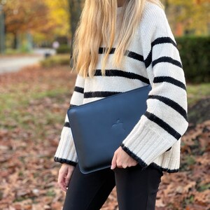 K&ouml;nnte beinhalten: Eine Frau in einem schwarz-wei&szlig; gestreiften Pullover h&auml;lt eine dunkelblaue Laptop-H&uuml;lle mit einem Apple-Logo.