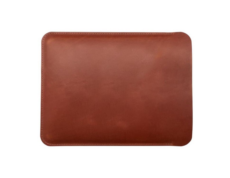 K&ouml;nnte beinhalten: Eine rechteckige, braune Lederh&uuml;lle mit abgerundeten Ecken. Die H&uuml;lle ist einfarbig und scheint an den R&auml;ndern gen&auml;ht zu sein. Das Leder hat eine glatte, matte Oberfl&auml;che. Die H&uuml;lle ist f&uuml;r ein Tablet oder einen Laptop konzipiert.