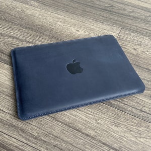 K&ouml;nnte beinhalten: Eine dunkelblaue Laptoptasche aus Leder mit einem schwarzen Apple-Logo.
