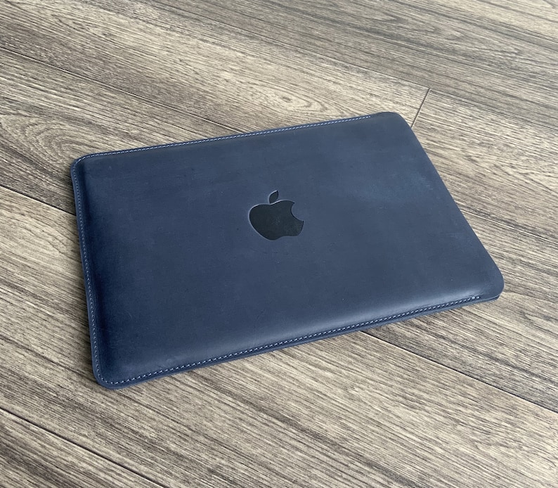 K&ouml;nnte beinhalten: Eine dunkelblaue Laptoptasche aus Leder mit einem schwarzen Apple-Logo.