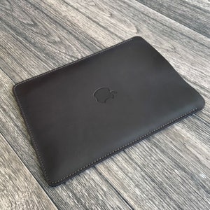 May include: A dark brown leather laptop sleeve with a stitched edge and an embossed Apple logo.