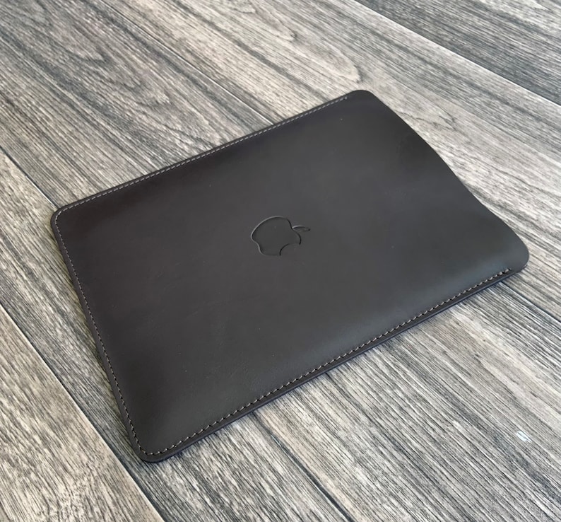 May include: A dark brown leather laptop sleeve with a stitched edge and an embossed Apple logo.