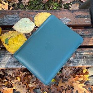 May include: A teal blue leather laptop sleeve with an Apple logo embossed on the front.