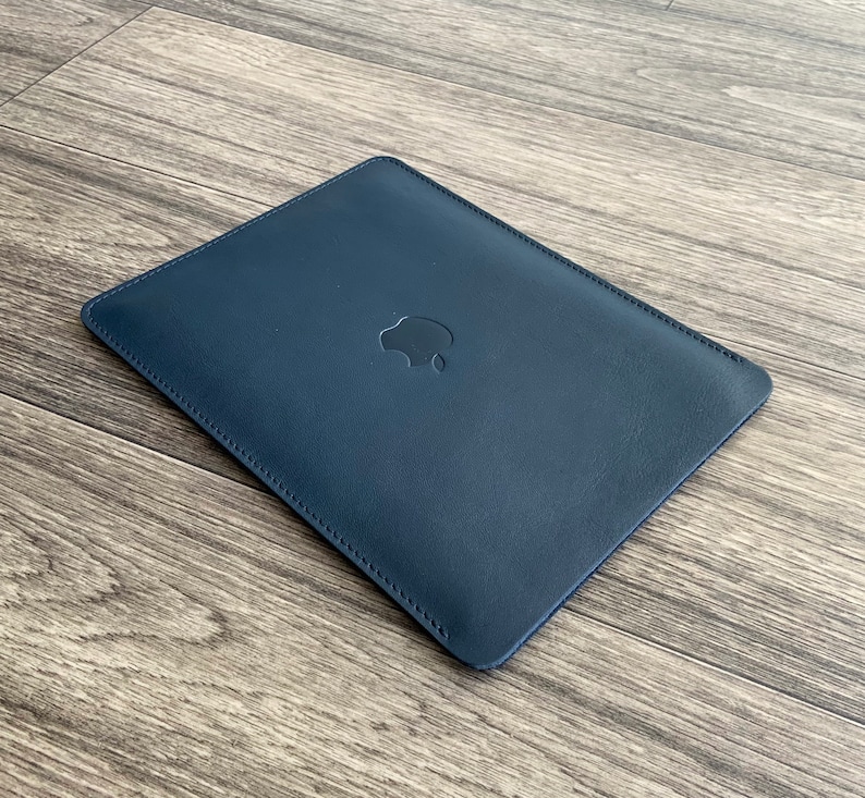 May include: A dark blue leather laptop sleeve with a subtle stitched design and an embossed Apple logo.