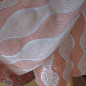 May include: A fabric textile featuring a repeating wavy pattern in shades of peach and white. The design consists of alternating vertical bands of textured peach and smooth white lines that create a flowing, rhythmic visual effect across the surface.