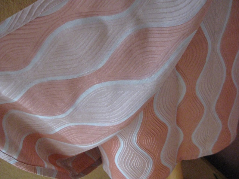 May include: A fabric textile featuring a repeating wavy pattern in shades of peach and white. The design consists of alternating vertical bands of textured peach and smooth white lines that create a flowing, rhythmic visual effect across the surface.