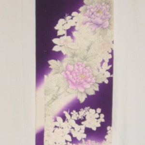 May include: A long, rectangular textile with a deep purple background, adorned with a floral pattern. The design features large, light purple and pink peonies, and white wisteria-like flowers. The fabric has a gradient effect.