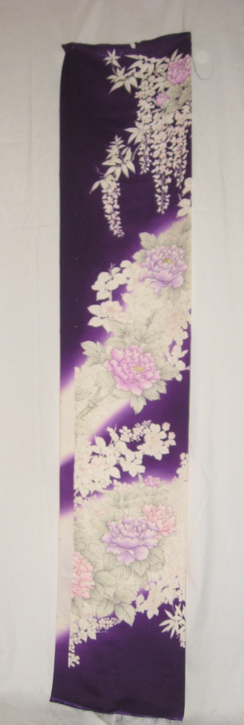 May include: A long, rectangular textile with a deep purple background, adorned with a floral pattern. The design features large, light purple and pink peonies, and white wisteria-like flowers. The fabric has a gradient effect.