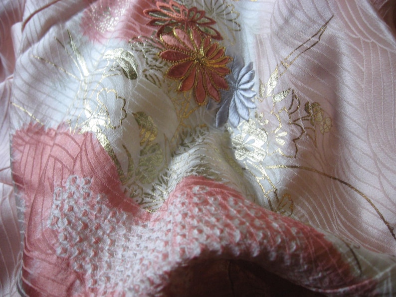 May include: A close-up of a pink and white fabric with gold and silver embroidery. The fabric has a delicate floral pattern with a textured surface.