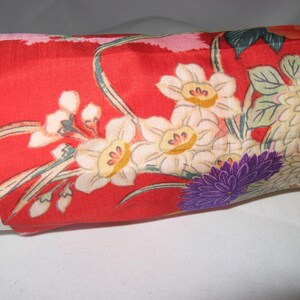 May include: Red fabric with a floral pattern featuring white, yellow, and purple flowers. The fabric has a silky texture.