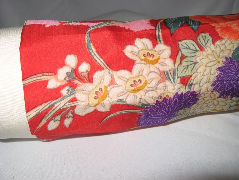 May include: Red fabric with a floral pattern featuring white, yellow, and purple flowers. The fabric has a silky texture.