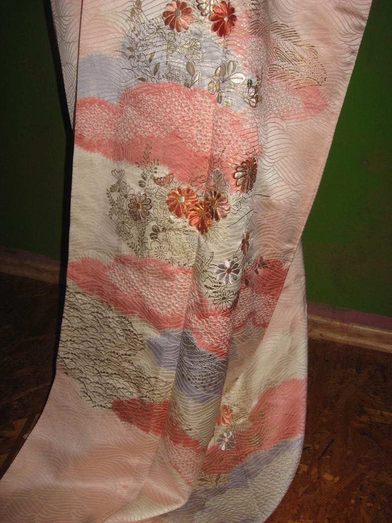 May include: A pink and white silk kimono with gold and silver embroidery of flowers and waves. The kimono has a traditional Japanese design.