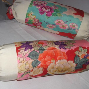 May include: Two white fabric cylindrical pillows with colorful floral patterns. The pillows have purple ties at the ends.